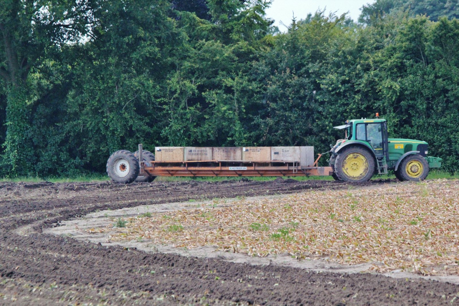 Tracteur attelé à une remorque plateau en bordure d'une parcelle travaillée